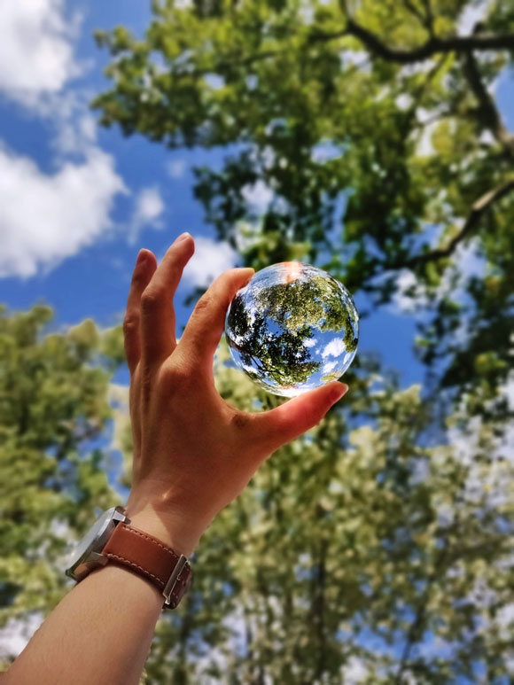 main tendant une bille de verre sur fond de nature pour symboliser la planète terre et l'écologie